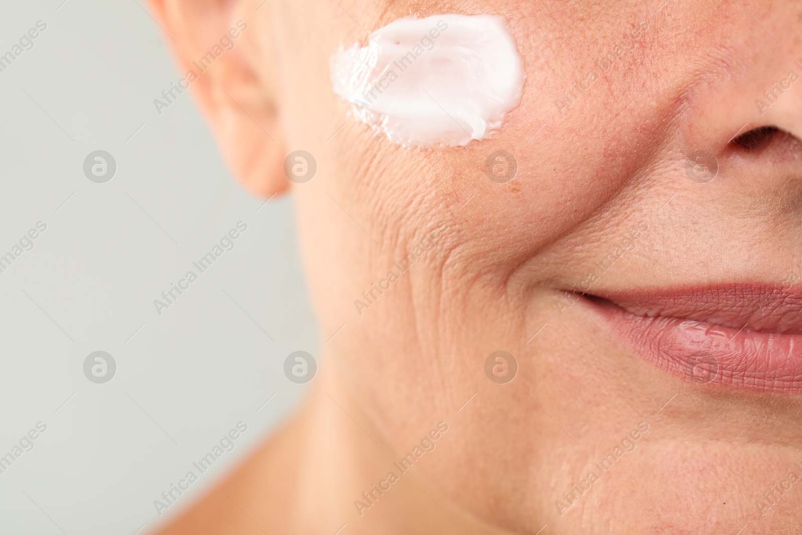 Photo of Senior woman with face cream on light background, closeup