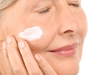 Senior woman applying face cream on light background, closeup