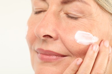 Photo of Senior woman applying face cream on light background, closeup