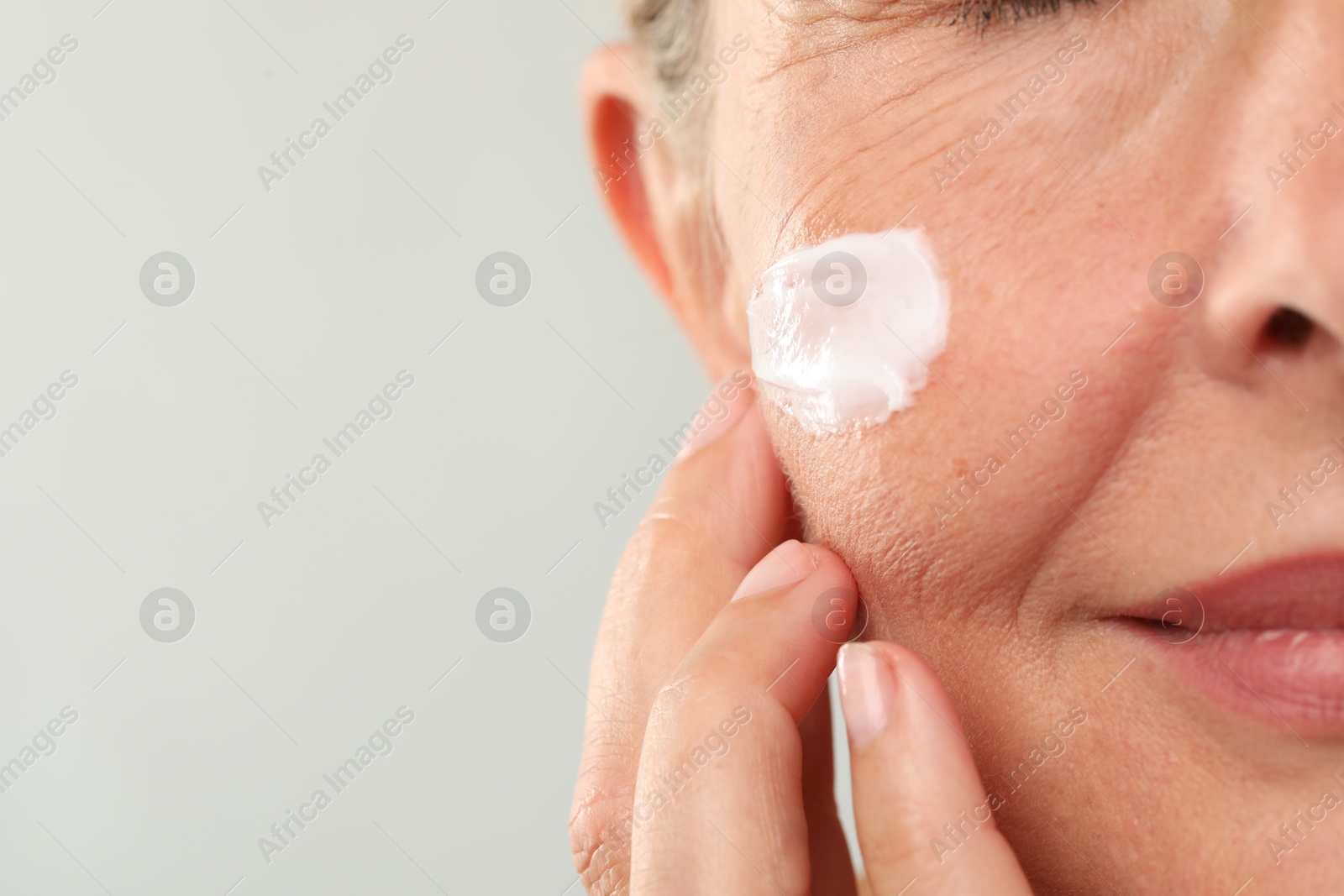 Photo of Senior woman with face cream on light background, closeup. Space for text