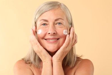 Photo of Senior woman with face cream on beige background