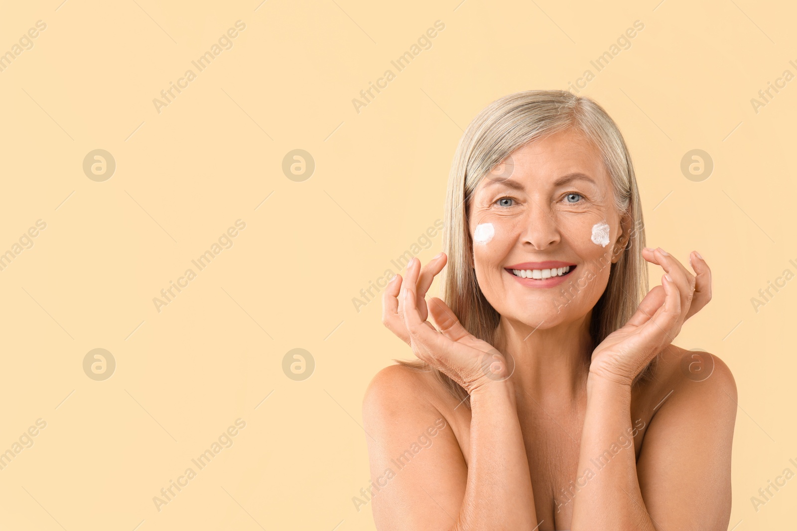 Photo of Senior woman with face cream on beige background. Space for text