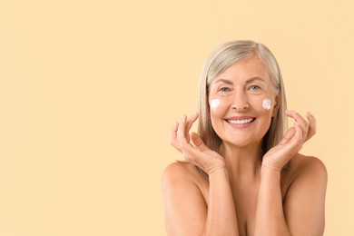 Photo of Senior woman with face cream on beige background. Space for text