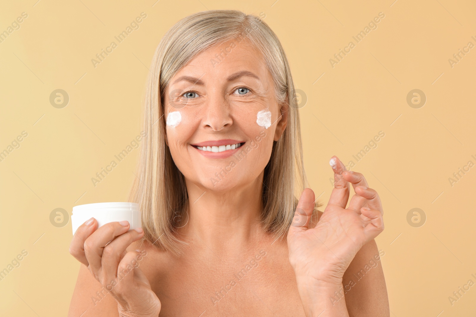 Photo of Senior woman with face cream on beige background