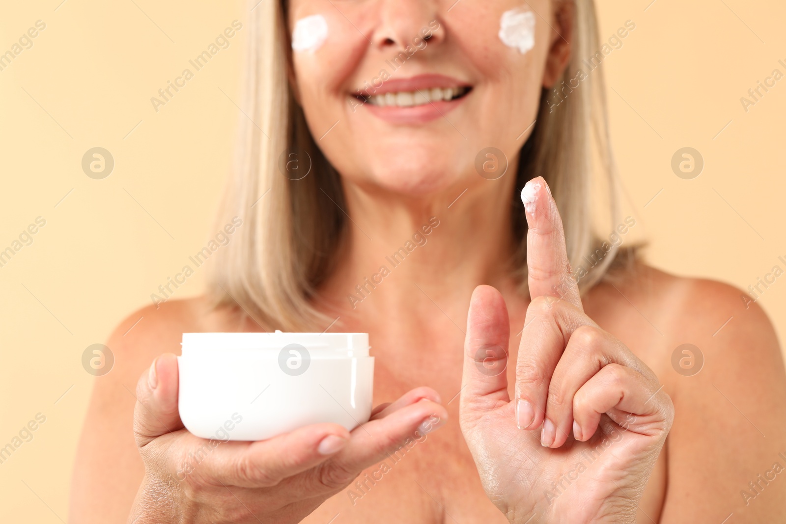 Photo of Senior woman with face cream on beige background, closeup