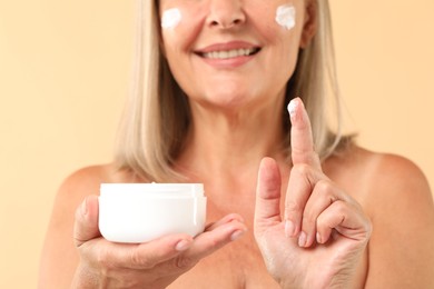 Photo of Senior woman with face cream on beige background, closeup