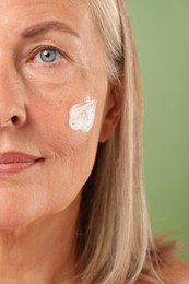 Photo of Senior woman with face cream on green background, closeup