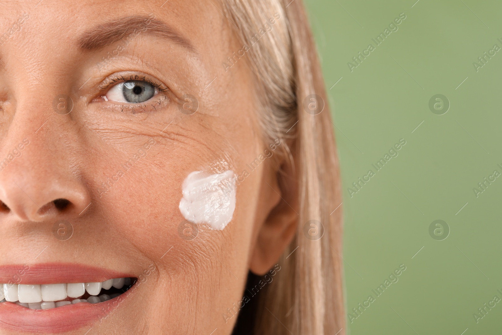 Photo of Senior woman with face cream on green background, closeup