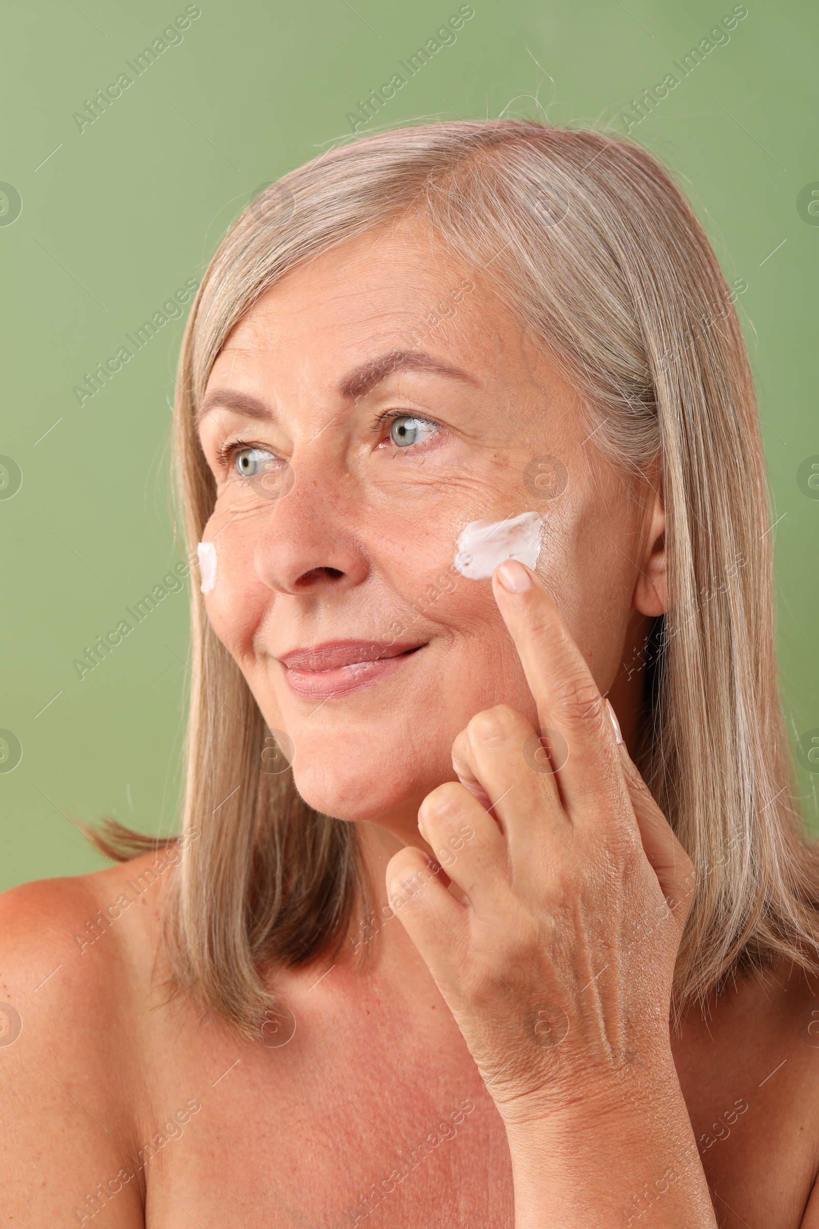 Photo of Senior woman applying face cream on green background