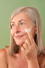 Senior woman applying face cream on green background