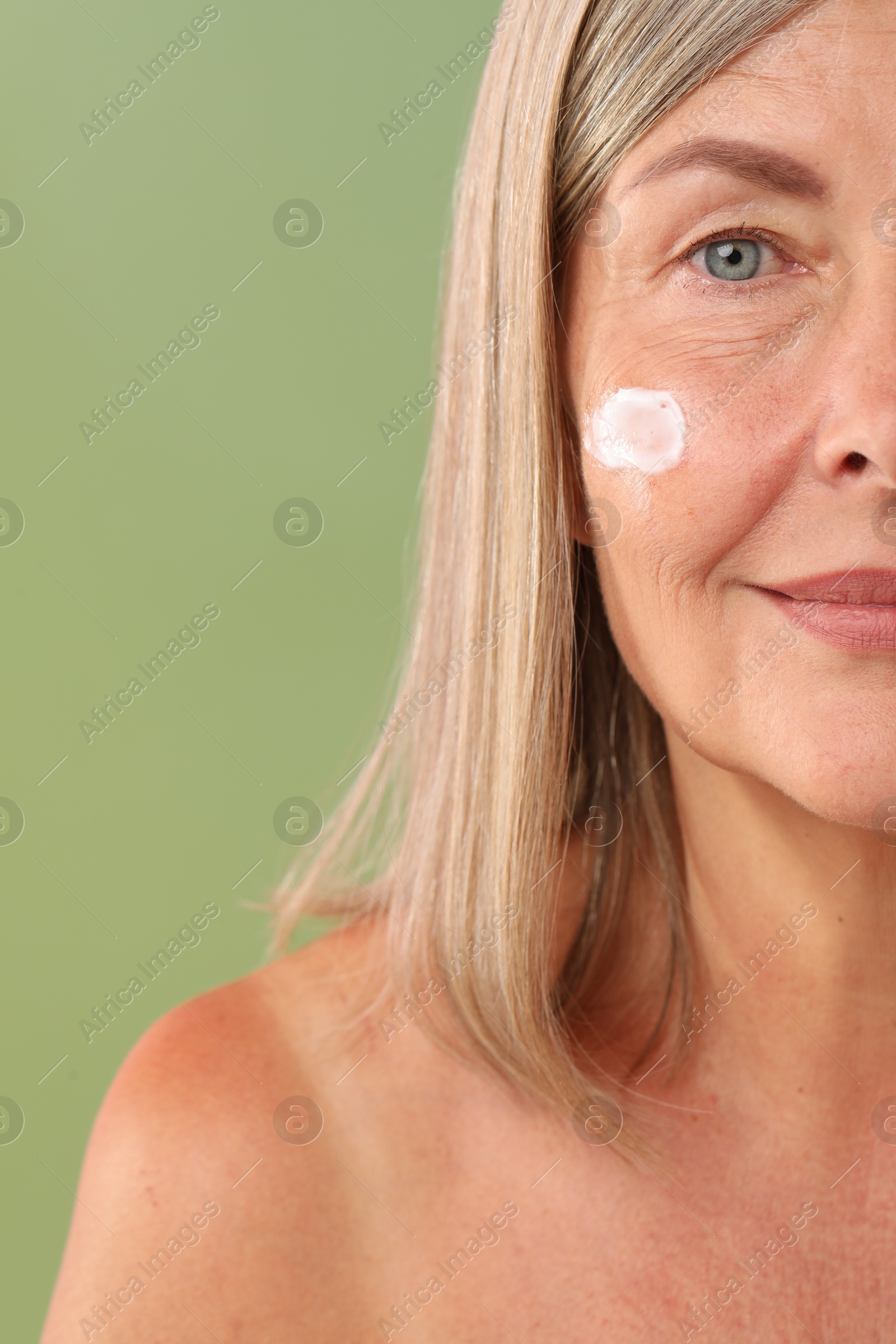 Photo of Senior woman with face cream on green background, closeup