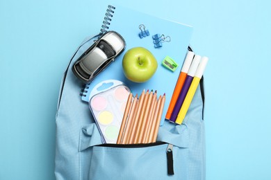 Photo of Backpack with different school stationery on light blue background, top view