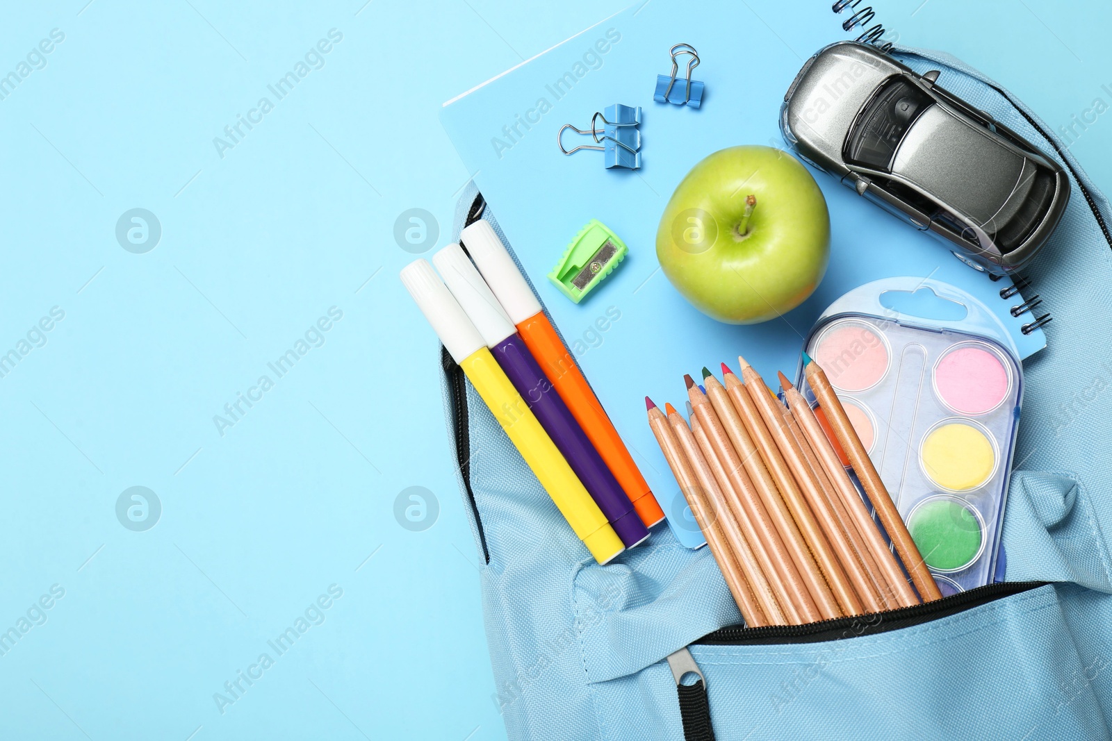 Photo of Backpack with different school stationery on light blue background, top view. Space for text