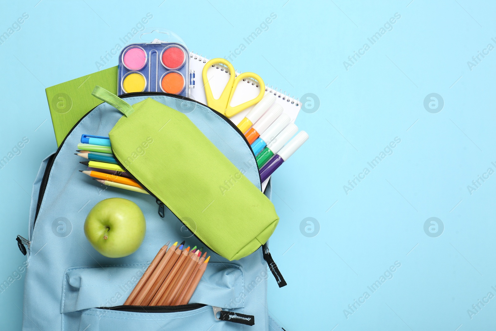 Photo of Backpack with different school stationery on light blue background, top view. Space for text