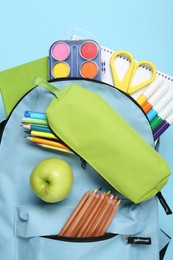 Photo of Backpack with different school stationery on light blue background, top view