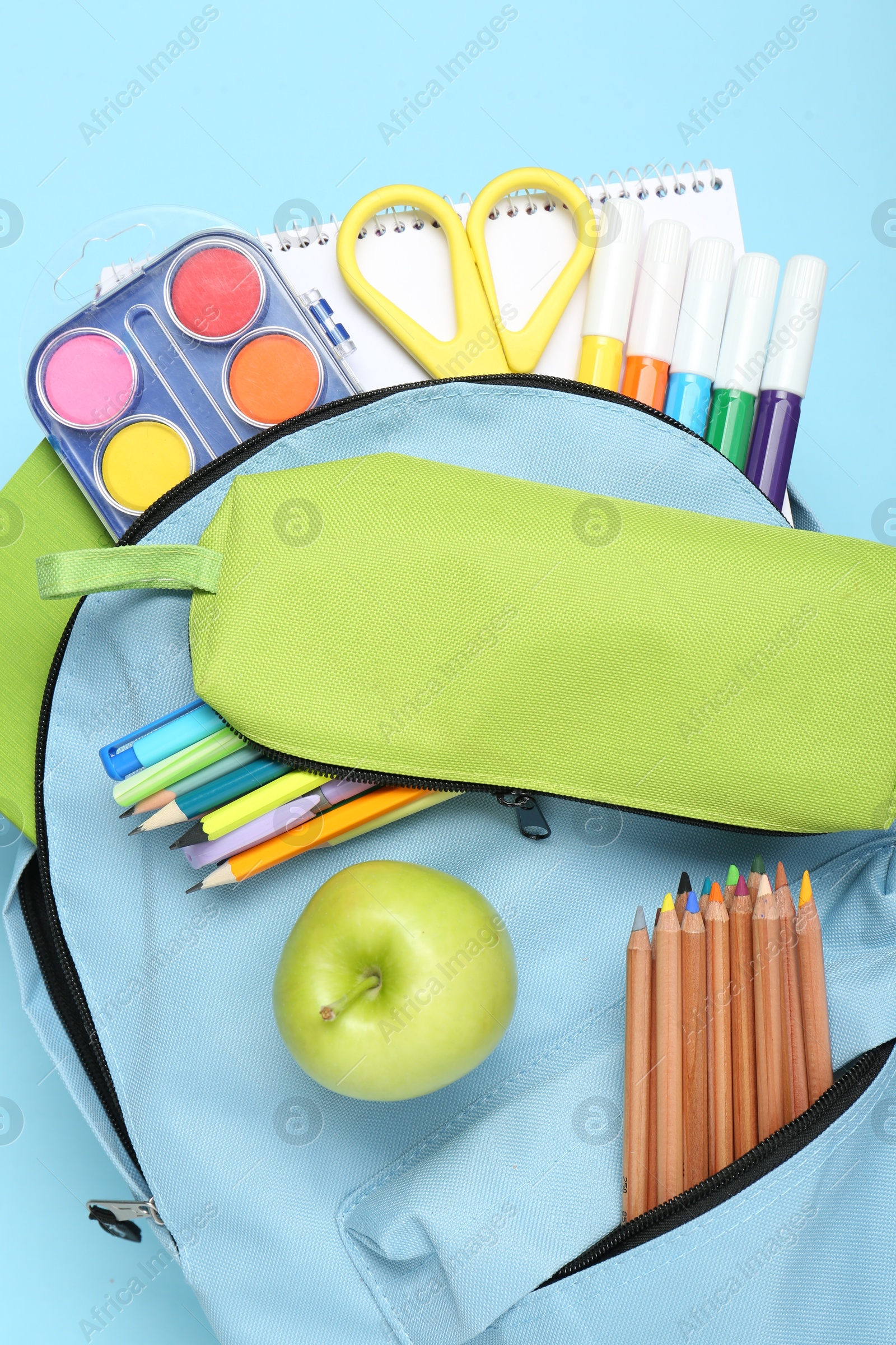 Photo of Backpack with different school stationery on light blue background, top view