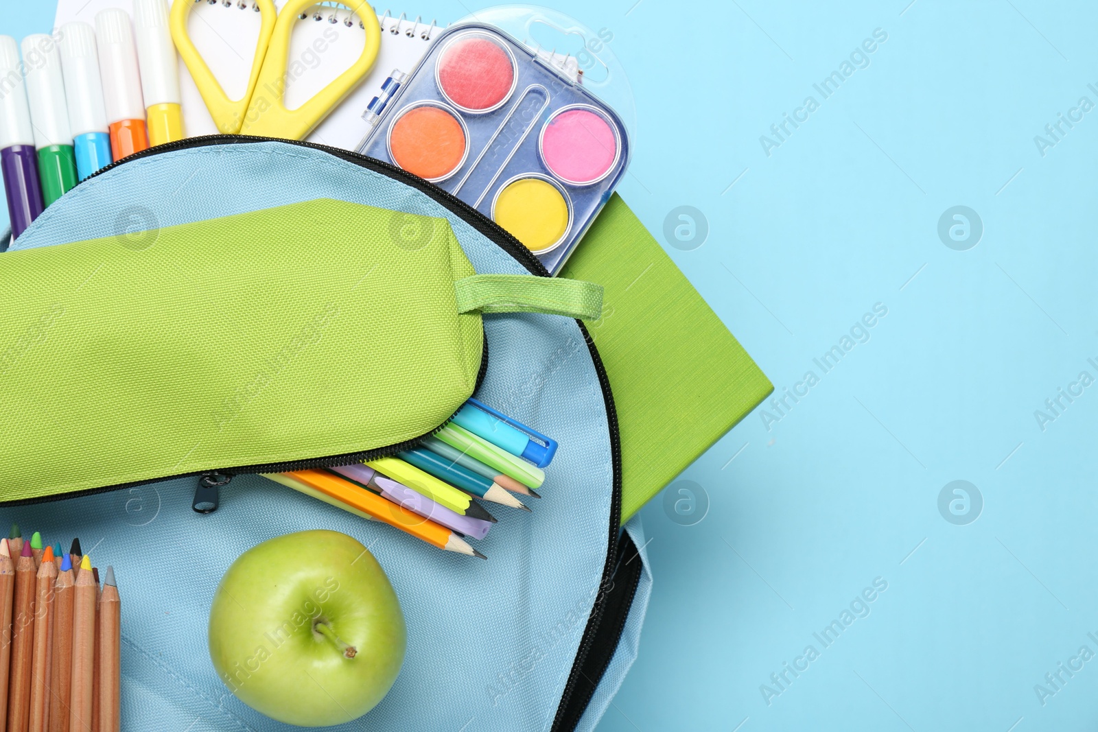 Photo of Backpack with different school stationery on light blue background, top view. Space for text