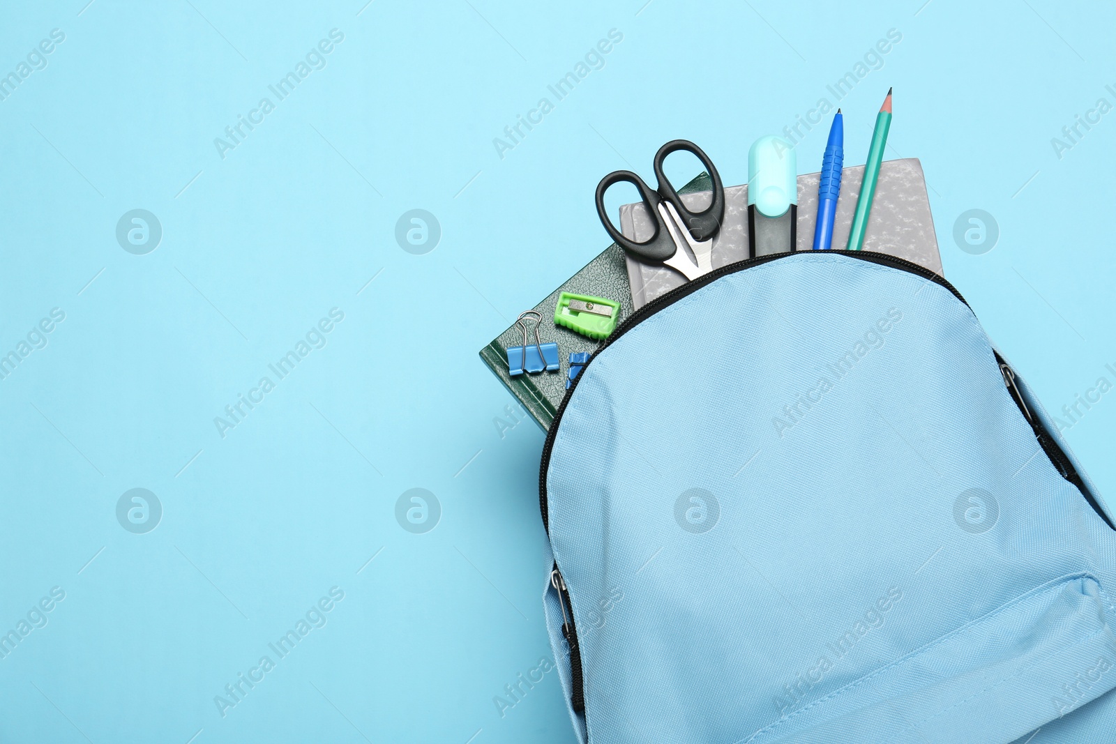 Photo of Backpack with different school stationery on light blue background, top view. Space for text