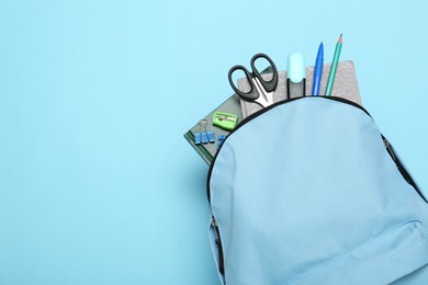 Backpack with different school stationery on light blue background, top view. Space for text