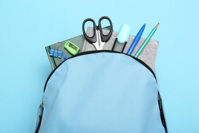 Backpack with different school stationery on light blue background, top view