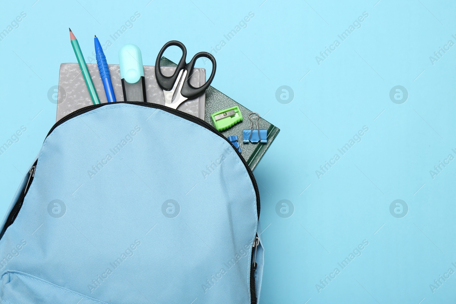 Photo of Backpack with different school stationery on light blue background, top view. Space for text