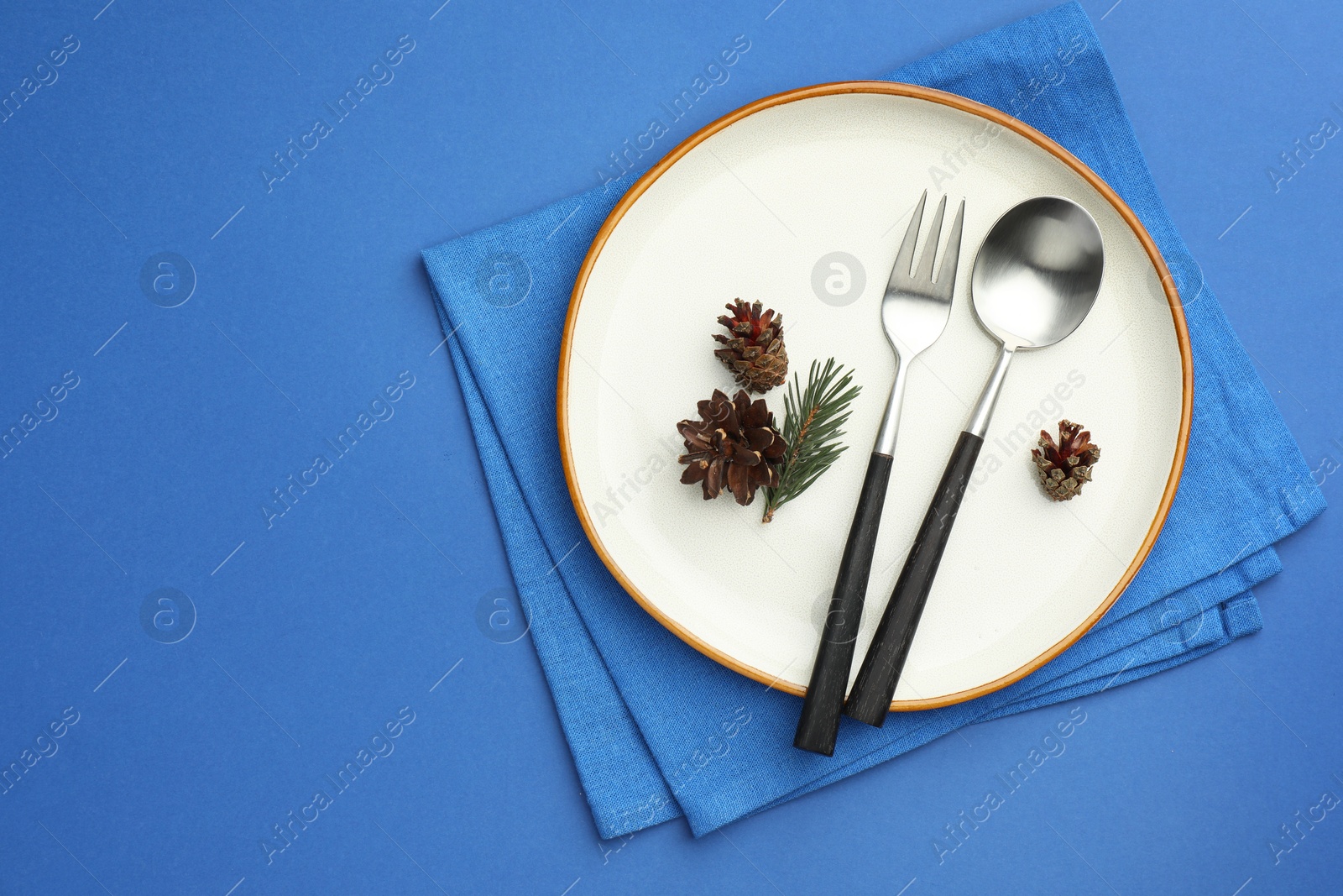 Photo of Beautiful Christmas setting with plate, cutlery and cones on blue table, top view. Space for text