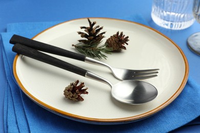 Photo of Beautiful Christmas setting with plate, cutlery and cones on blue table