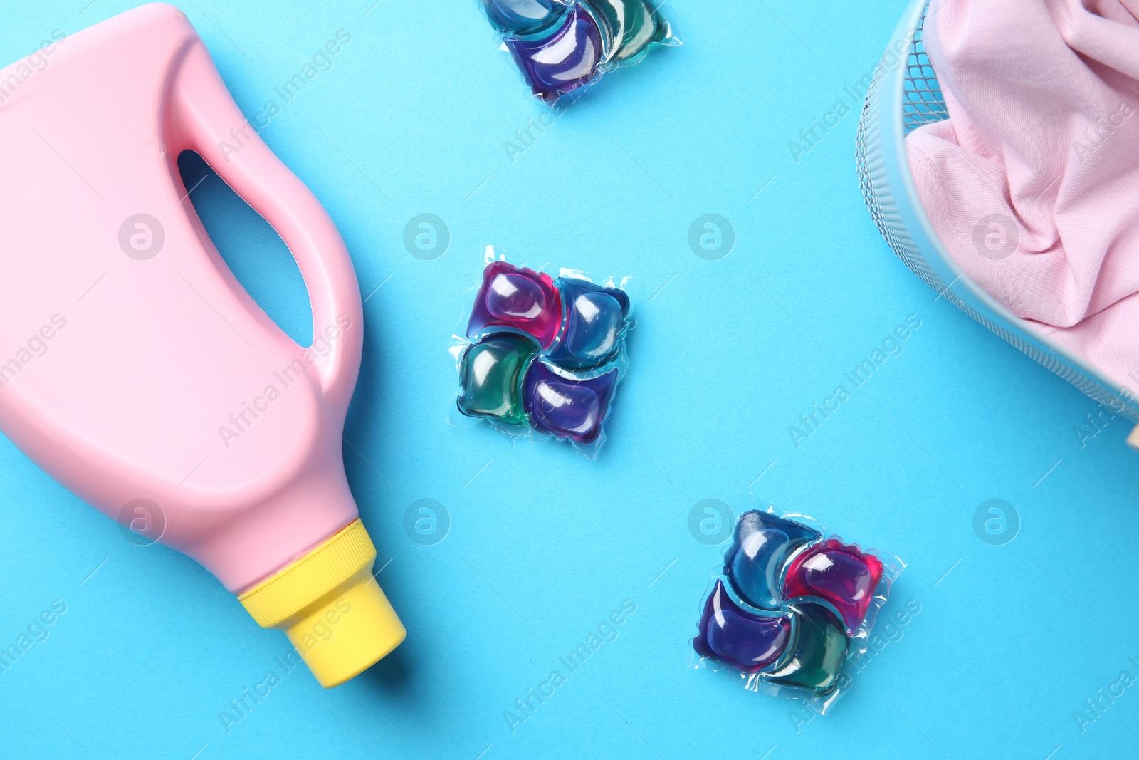 Photo of Basket with clothes, bottle of fabric softener and laundry detergent pods on blue background, flat lay