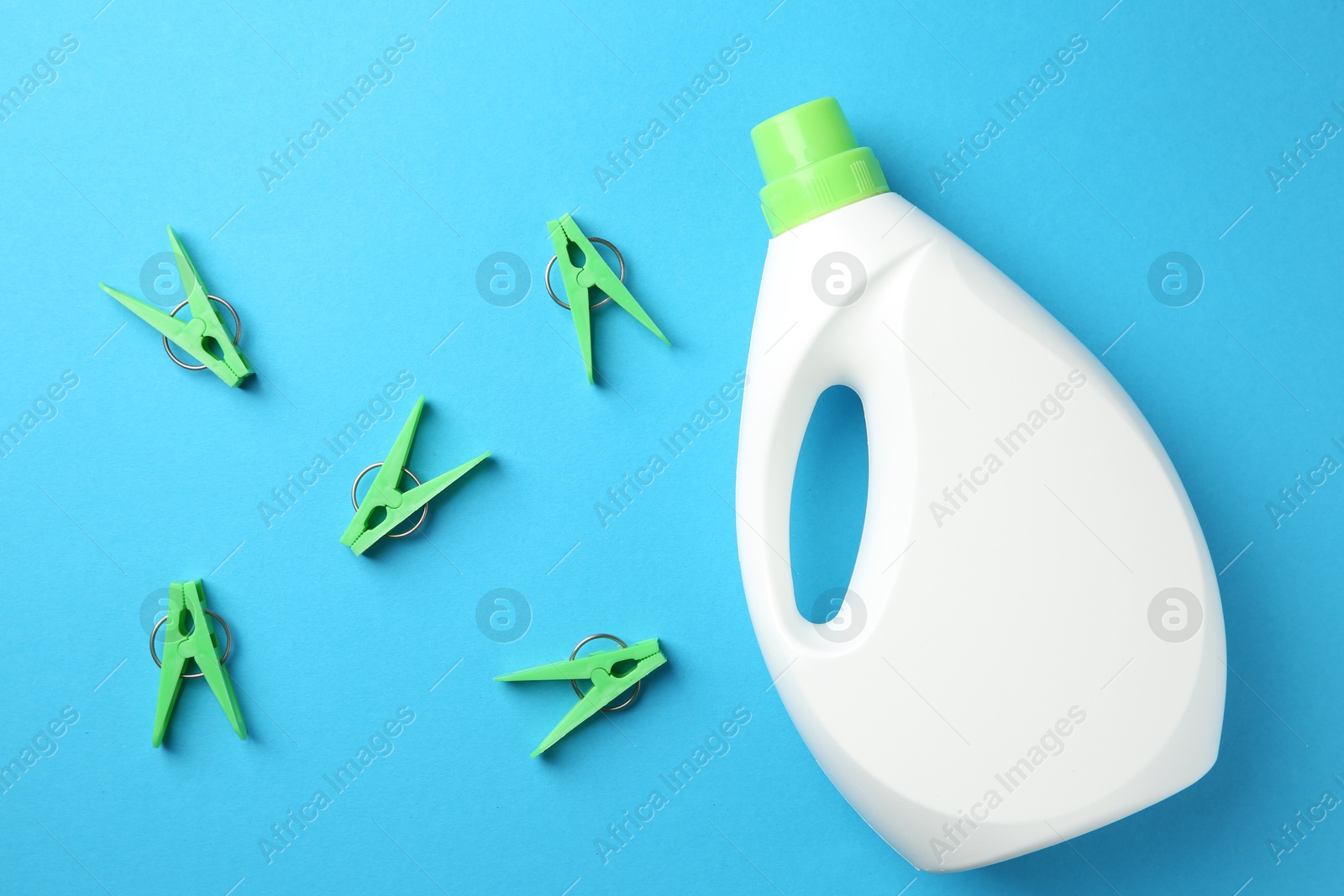 Photo of Bottle of laundry detergent and clothespins on blue background, flat lay