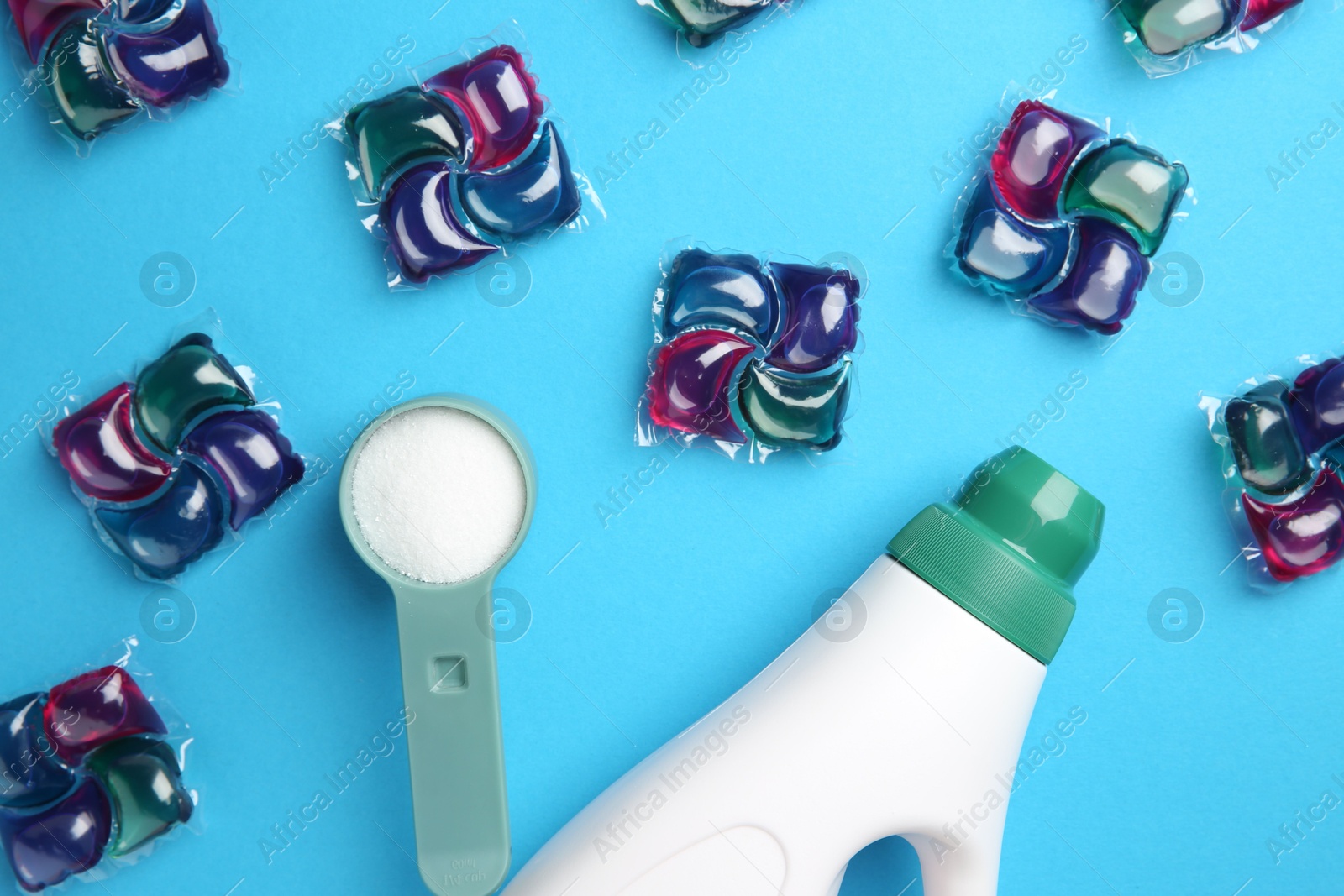 Photo of Bottle of fabric softener, laundry detergent pods and measuring scoop of washing powder on blue background, flat lay