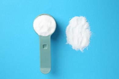 Measuring scoop with laundry powder on blue background, flat lay