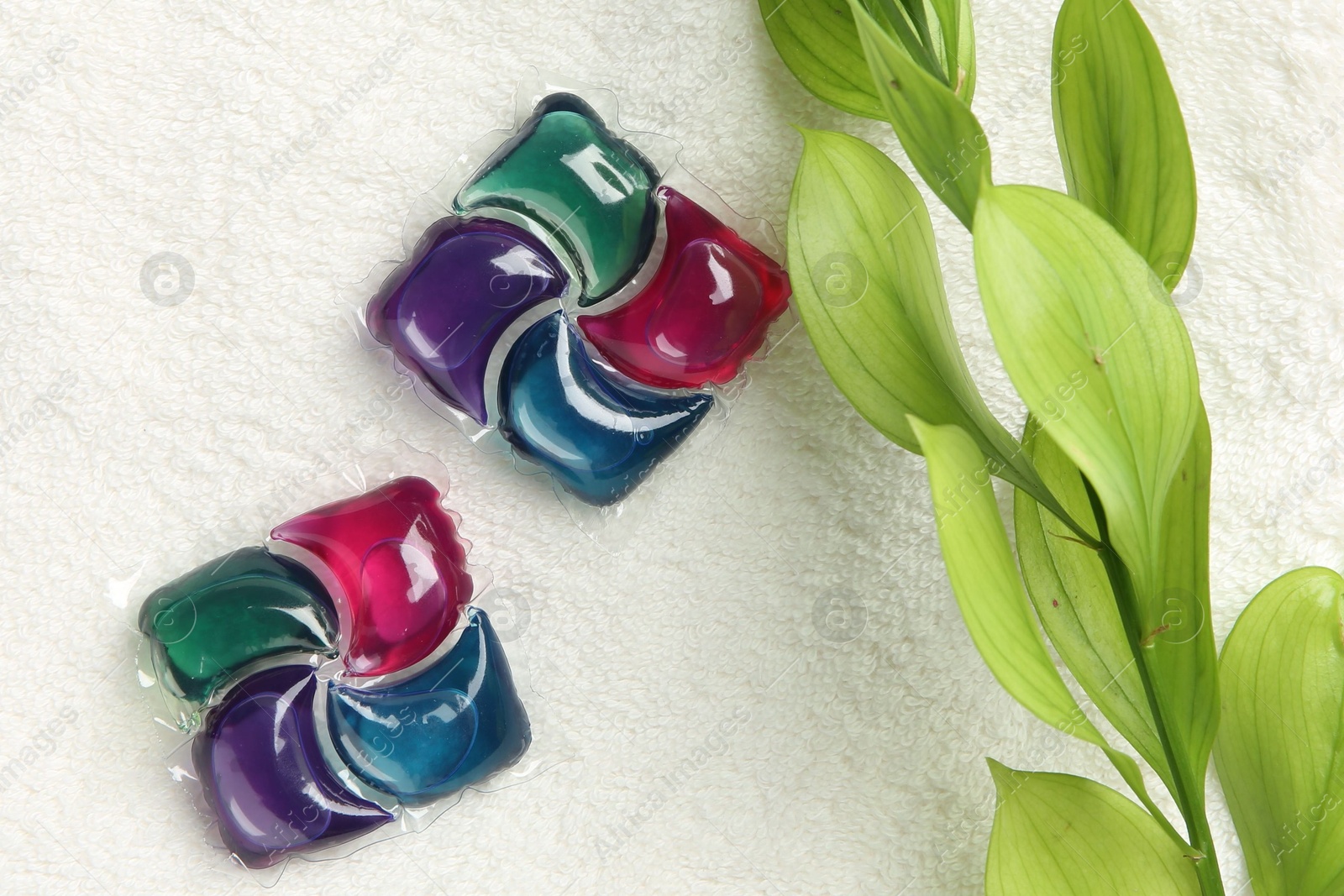 Photo of Laundry detergent pods and green branch on towel , flat lay