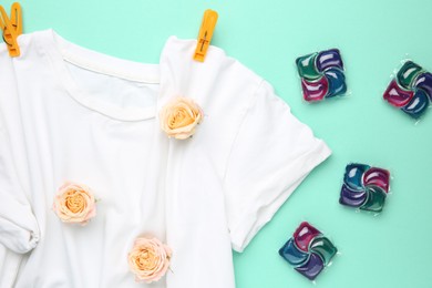 Photo of Laundry detergent pods, t-shirt, flowers and clothespins on turquoise background, flat lay