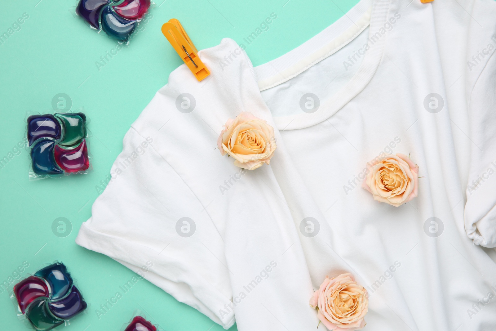 Photo of Laundry detergent pods, t-shirt, flowers and clothespins on turquoise background, flat lay