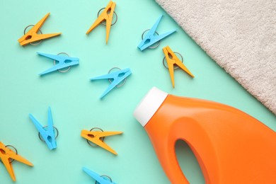 Photo of Bottle of laundry detergent, towel and many colorful clothespins on turquoise background, flat lay