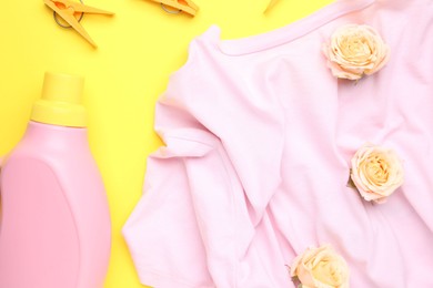 Photo of Bottle of laundry detergent, t-shirt, flowers and clothespins on yellow background, flat lay