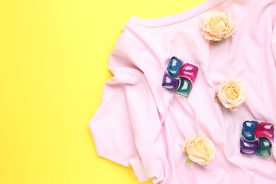 Photo of Laundry detergent pods, t-shirt and flowers on yellow background, flat lay. Space for text