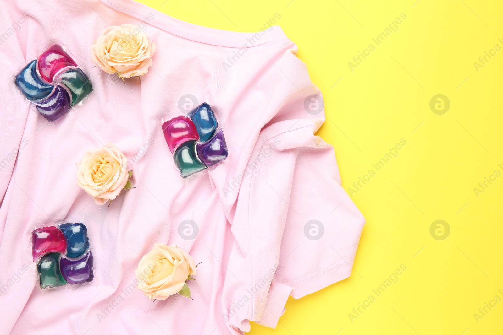 Photo of Laundry detergent pods, t-shirt and flowers on yellow background, flat lay. Space for text