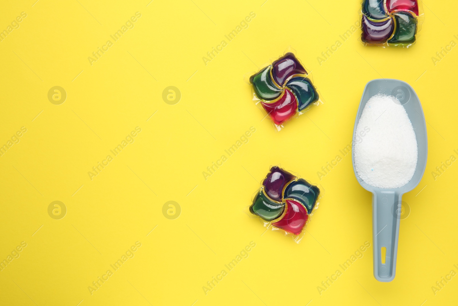 Photo of Laundry capsules and detergent powder on yellow background, flat lay. Space for text