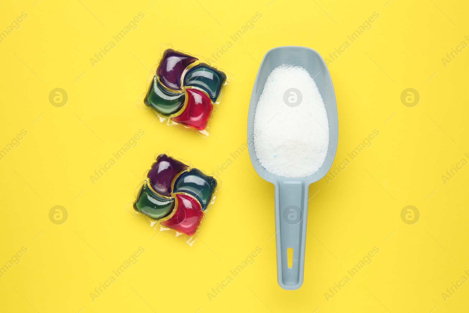 Photo of Laundry capsules and detergent powder on yellow background, flat lay