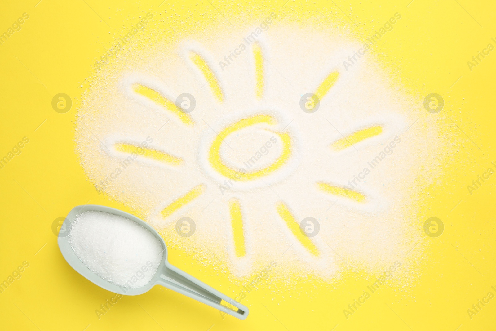 Photo of Measuring scoop and sun made with laundry powder on yellow background, flat lay