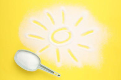 Photo of Measuring scoop and sun made with laundry powder on yellow background, flat lay