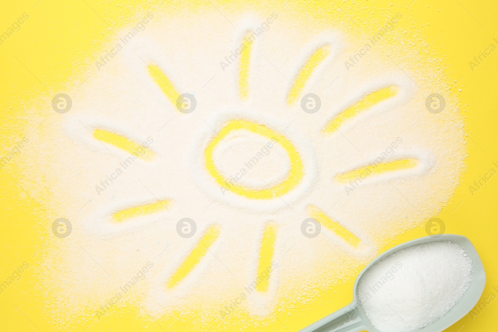 Photo of Measuring scoop and sun made with laundry powder on yellow background, flat lay