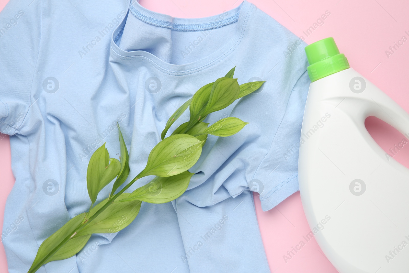 Photo of Bottle of laundry detergent, t-shirt and green branch on pink background, flat lay