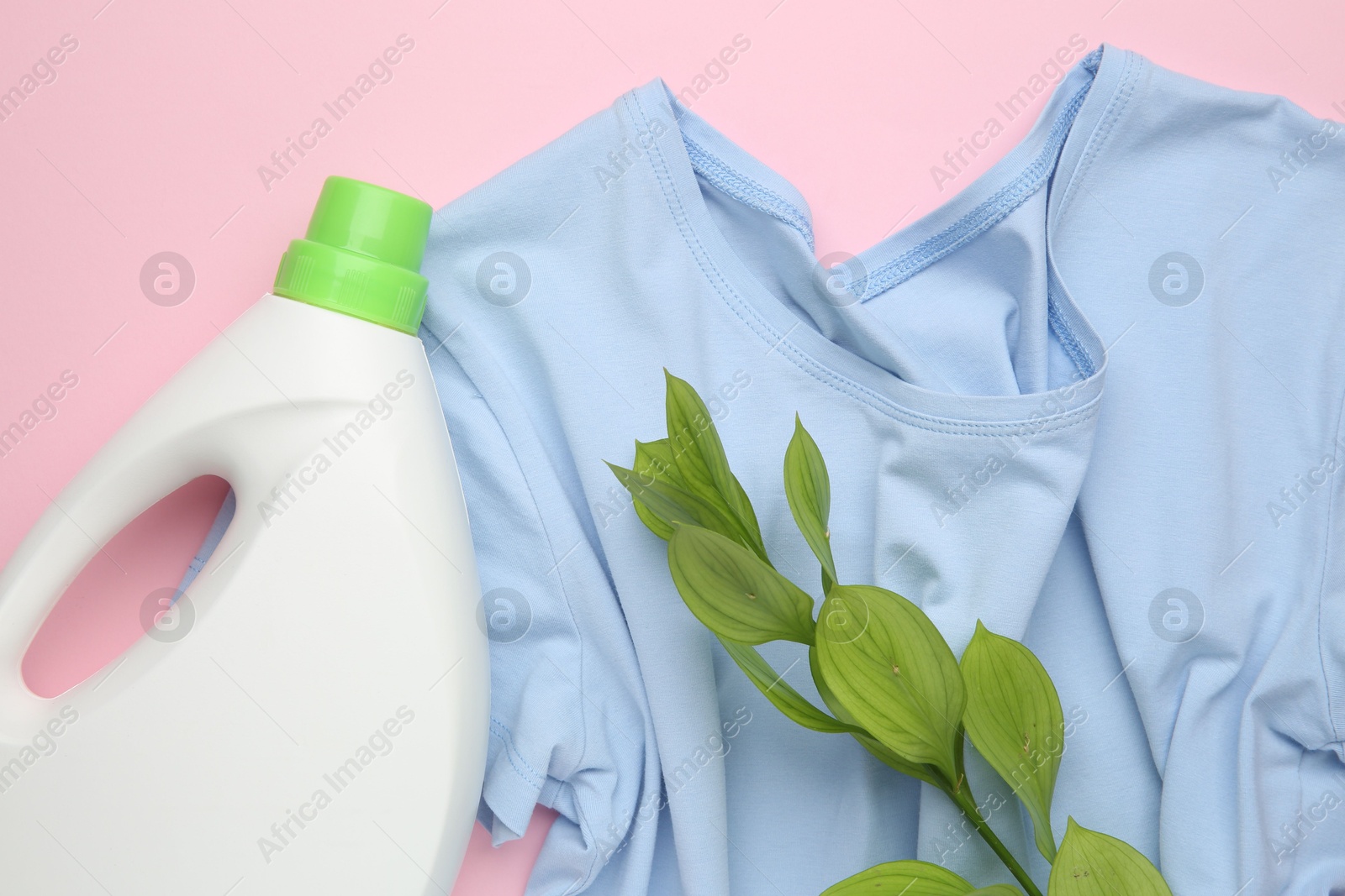 Photo of Bottle of laundry detergent, t-shirt and green branch on pink background, flat lay