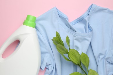 Photo of Bottle of laundry detergent, t-shirt and green branch on pink background, flat lay