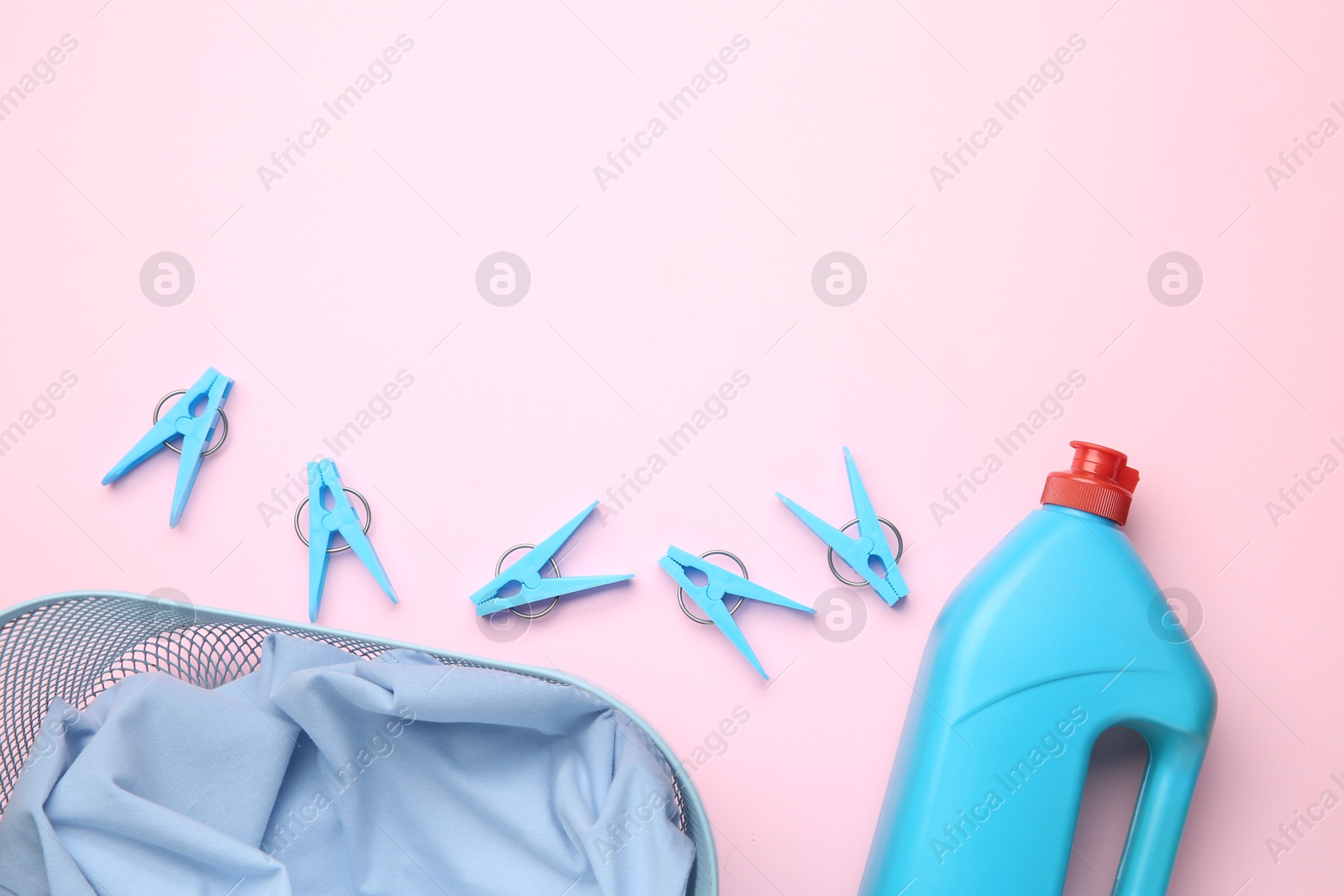 Photo of Basket with clothes, bottle laundry detergent and clothespins on pink background, flat lay. Space for text