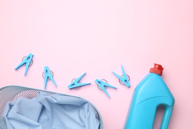 Photo of Basket with clothes, bottle laundry detergent and clothespins on pink background, flat lay. Space for text