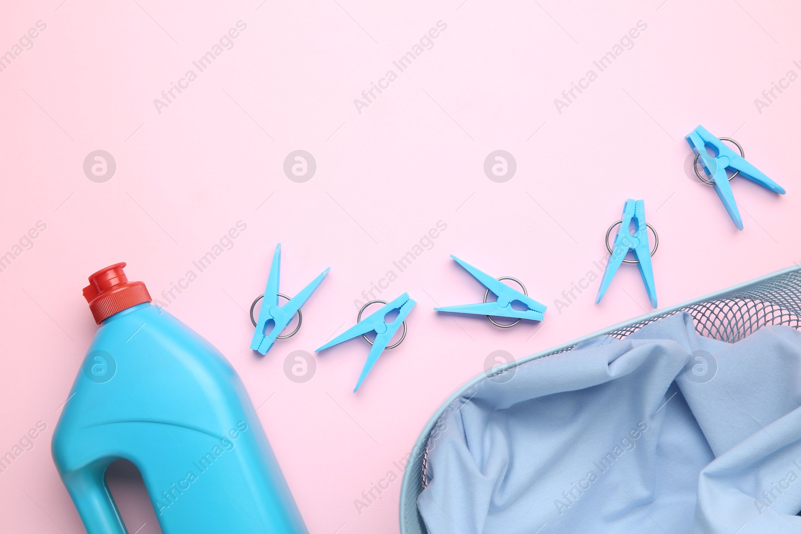 Photo of Basket with clothes, bottle laundry detergent and clothespins on pink background, flat lay. Space for text