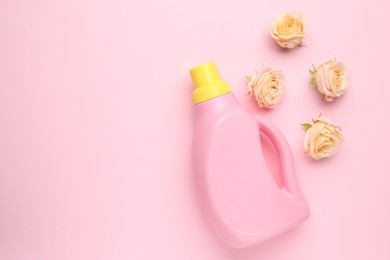 Photo of Bottle of laundry detergent and flowers on pink background, closeup. Space for text